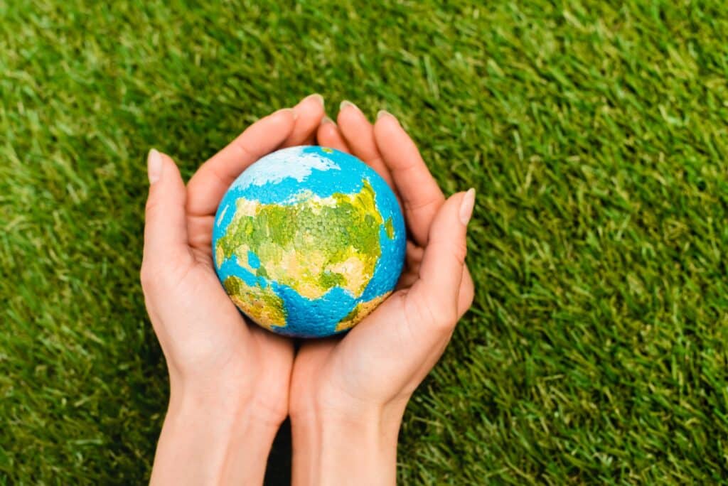 Cropped view of globe in female hands on green background, earth day concept